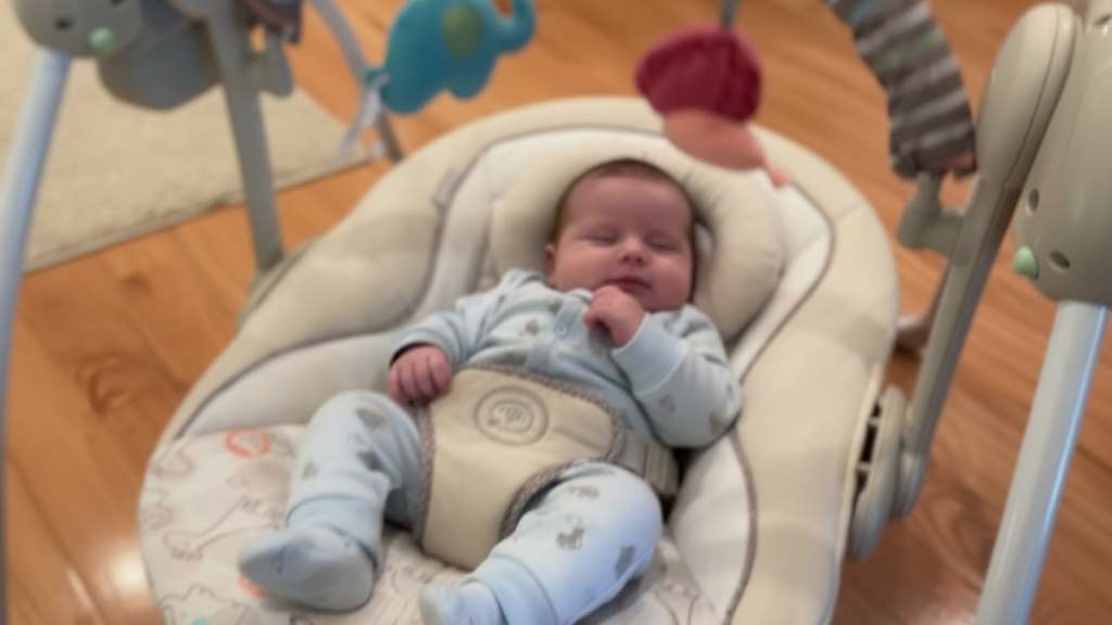 Infant relaxing in plush seat of compact baby swing with soothing multi-directional motion activated