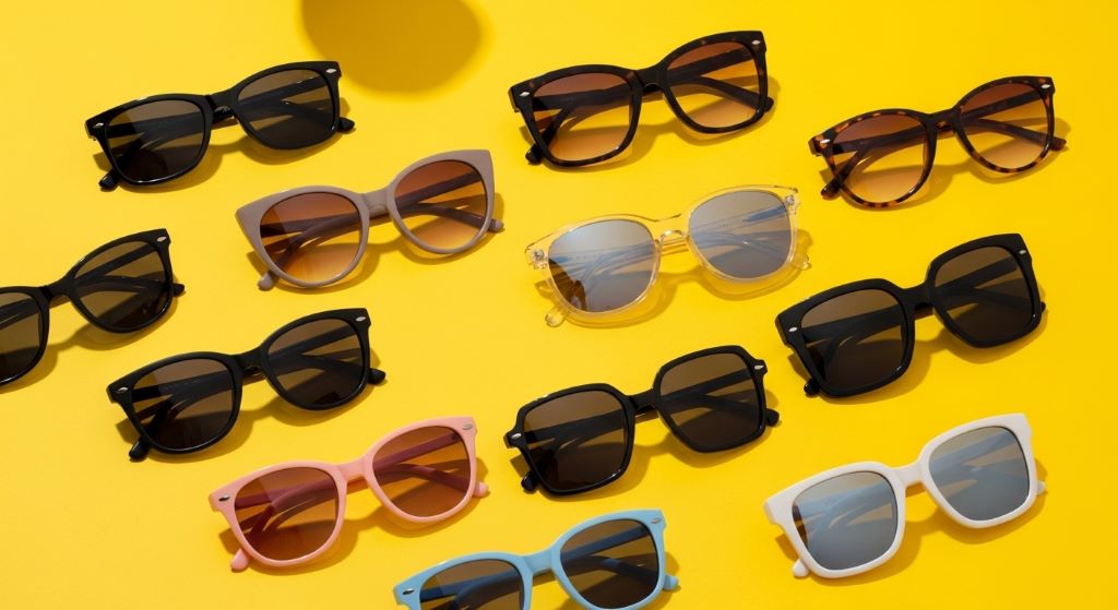 Flat lay of affordable luxury fashion sunglasses in various frame styles arranged on a bright yellow summer background