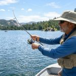 An angler wearing a wide-brim UPF 50+ fishing hat on a sunny lake, casting a fishing rod