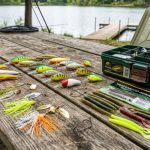 A colorful assortment of fishing lures including crankbaits, spinnerbaits, and soft plastics laid out on a wooden surface next to a tackle box