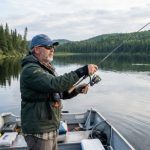 An angler wearing a wrist support brace while casting a fishing rod from a boat on a calm lake