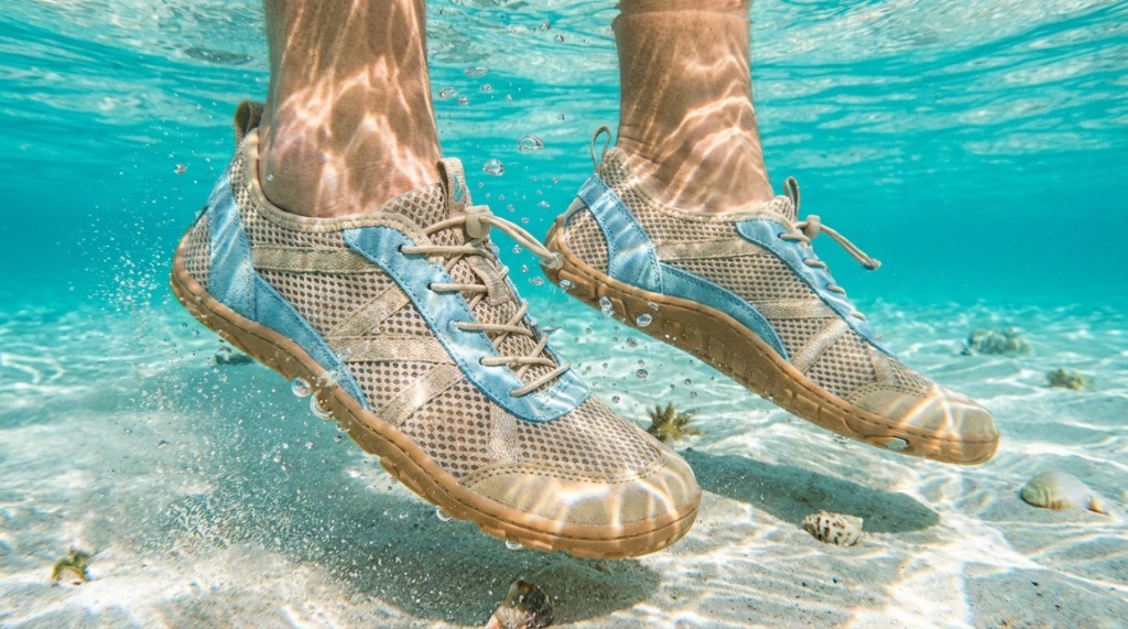 A close-up of lightweight saltwater fishing shoes wading through shallow, clear ocean water.
