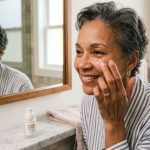 Woman applying anti-aging cream under her eye in a mirror.