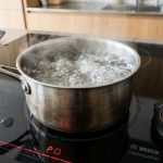 Digital timer beside boiling water on a sleek induction cooktop element.