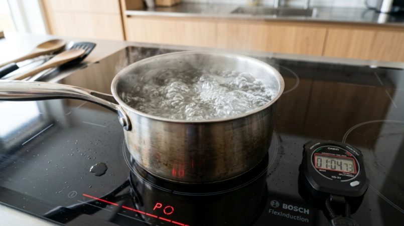 Digital timer beside boiling water on a sleek induction cooktop element.